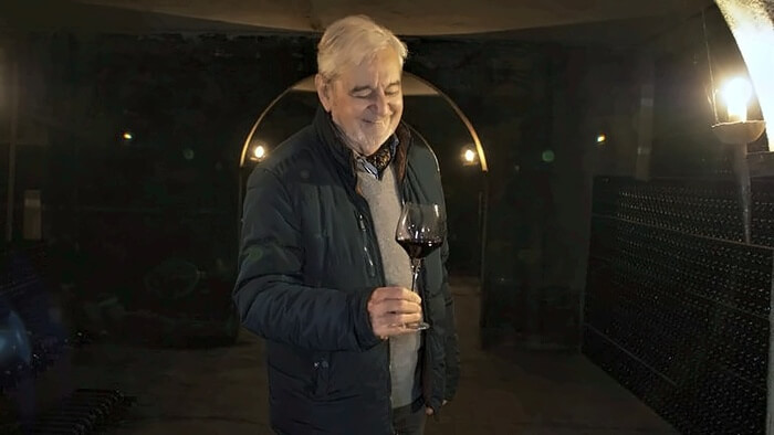 Jacques Pedro dégustant un vin dans le caveau des Domaines Pedro, entouré de bouteilles de grands millésimes du vignoble bordelais.