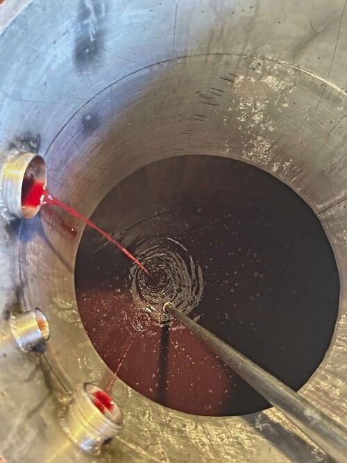 Remontage du vin rouge dans une cuve de vinification au sein du chai des Domaines Pedro, illustrant le savoir-faire viticole traditionnel du Médoc.